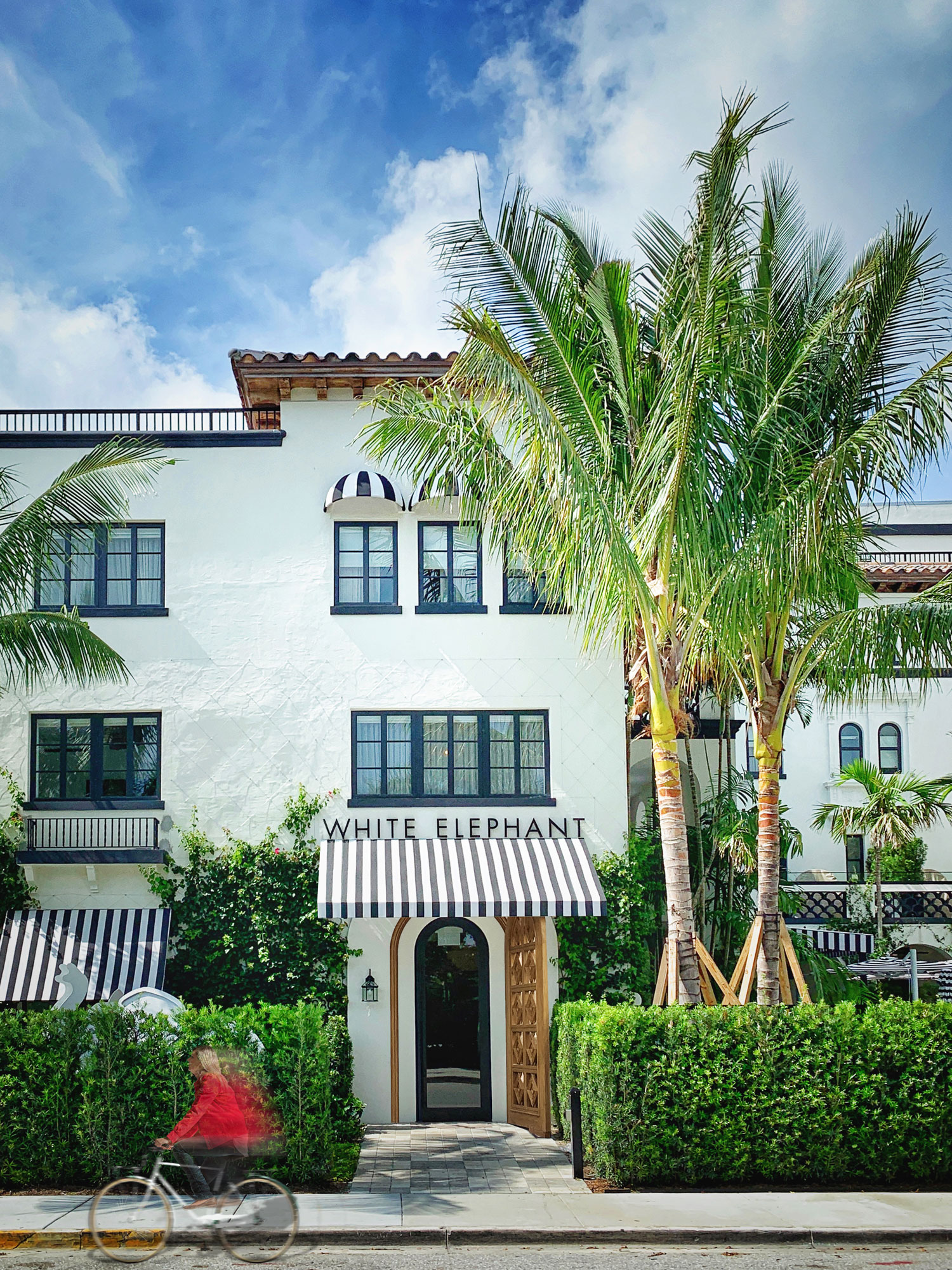 Front door of the White Elephant Palm Beach with a women bicycling by